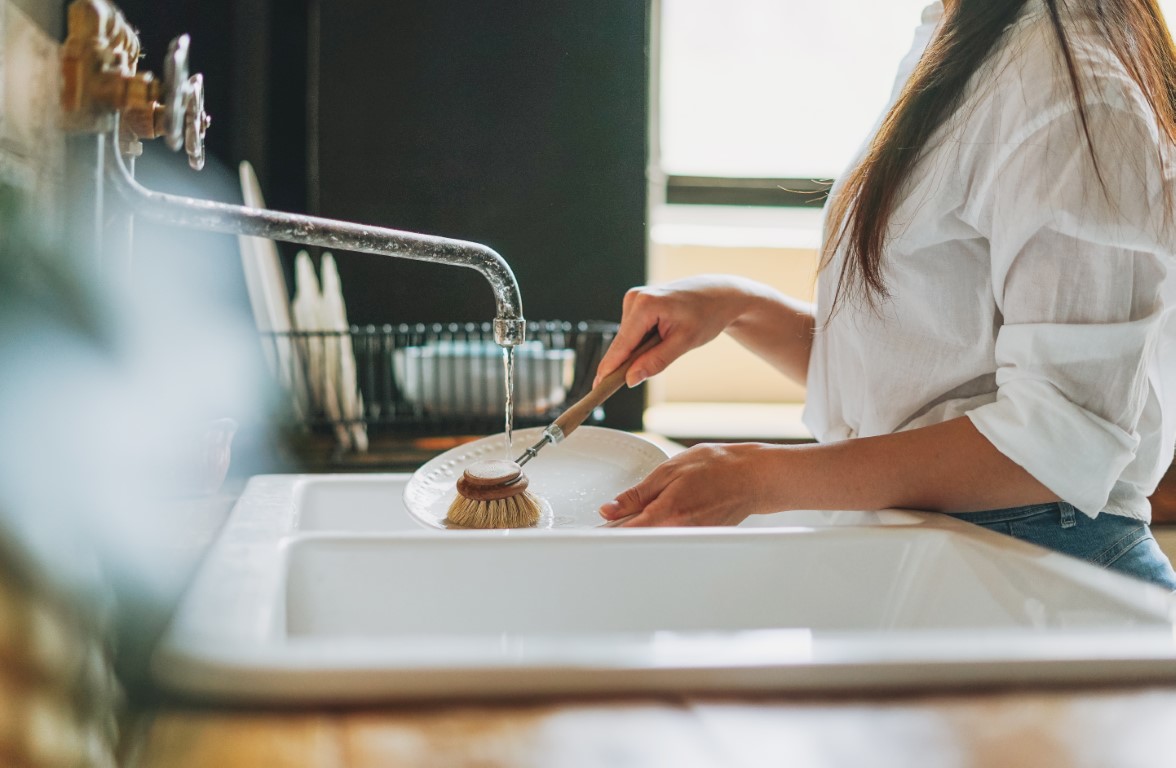 young-woman-washes-dishes-with-wooden-brush-with-n-4B585DJ