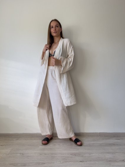 mušelínové kimono šaty v maslovej farbe  s mušelínovými dlhými letnými nohavicami na modelke pred bielou stenou