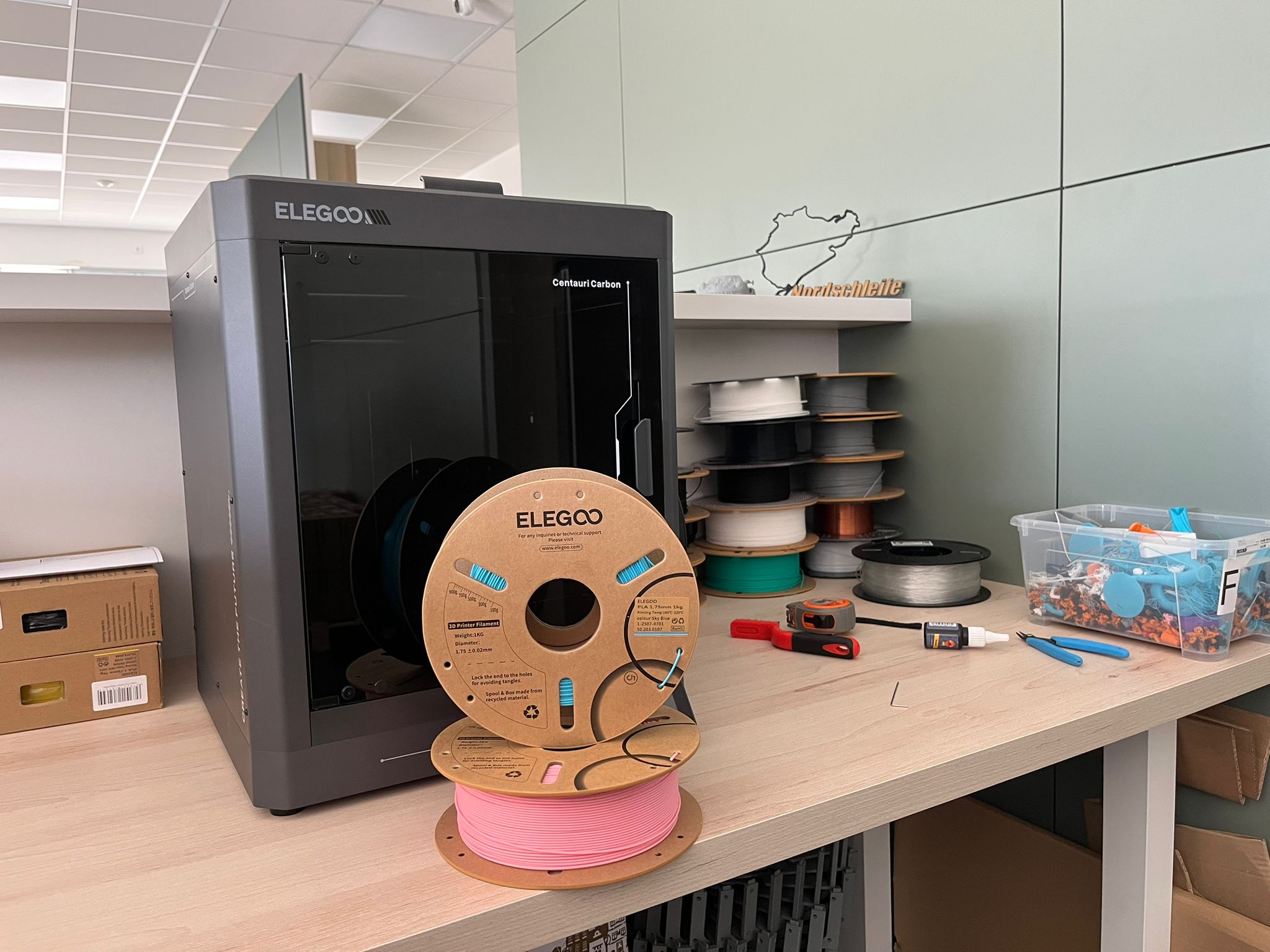 PLA filament FilamentyBrno na pracovním stole vedle běžící 3D tiskárny
