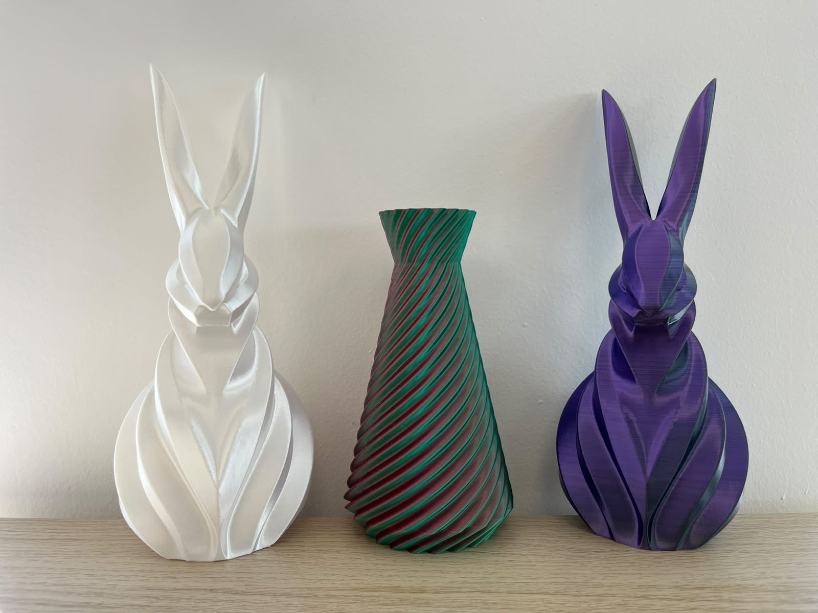 PLA Silk výrobky vytisknuté v showroomu FilamentyBrno — bílá lesklá figurka, dual-color spirálová váza a fialový dvoubarevný králík
