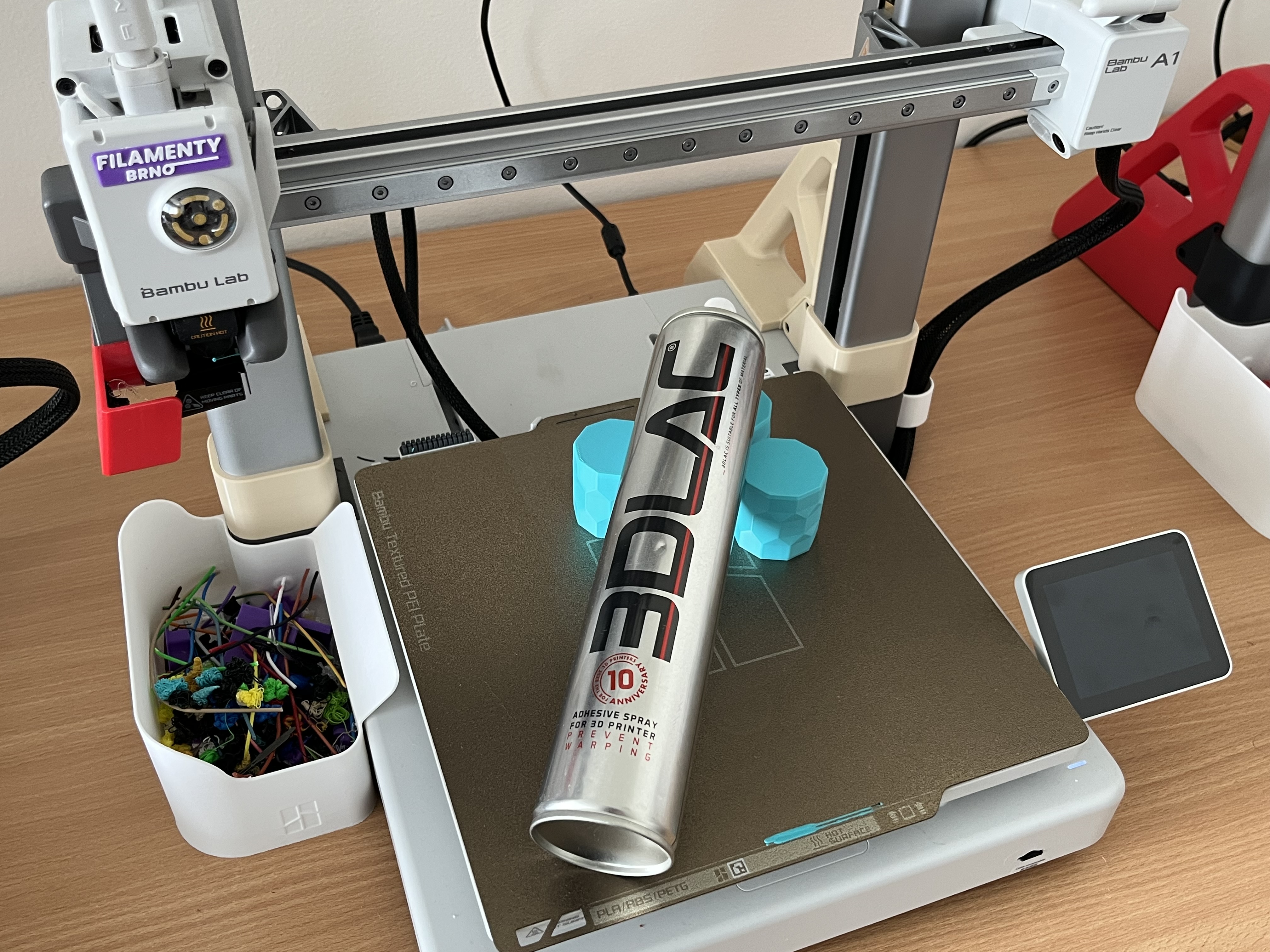 3DLAC adhezní sprej a úspěšně vytištěné PETG díly na texturované PEI podložce tiskárny Bambu Lab A1 v showroomu FilamentyBrno