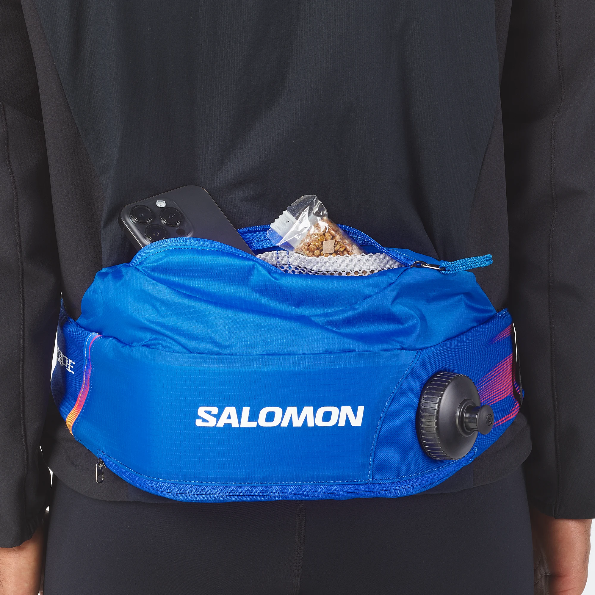 Ledvinka Salomon Thermobelt nošená vzadu na pase, v otevřené kapse je telefon a svačina