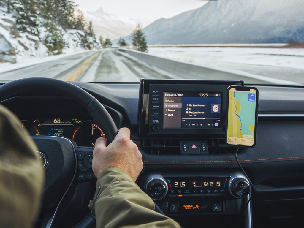 Řidič na zasněžené silnici, vedle displeje auta telefon s navigací v pouzdře (prodává se zvlášť) na nabíjecí hlavici (prodává se zvlášť) a lepicím držáku Quad Lock