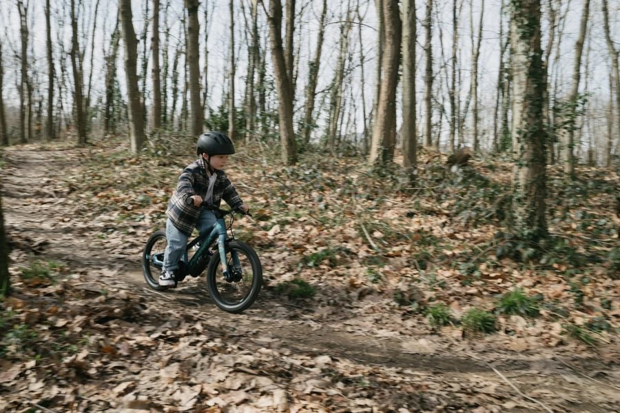 Dítě v helmě jede na dětském kole Orbea Kimu 16 po lesní cestě pokryté listím