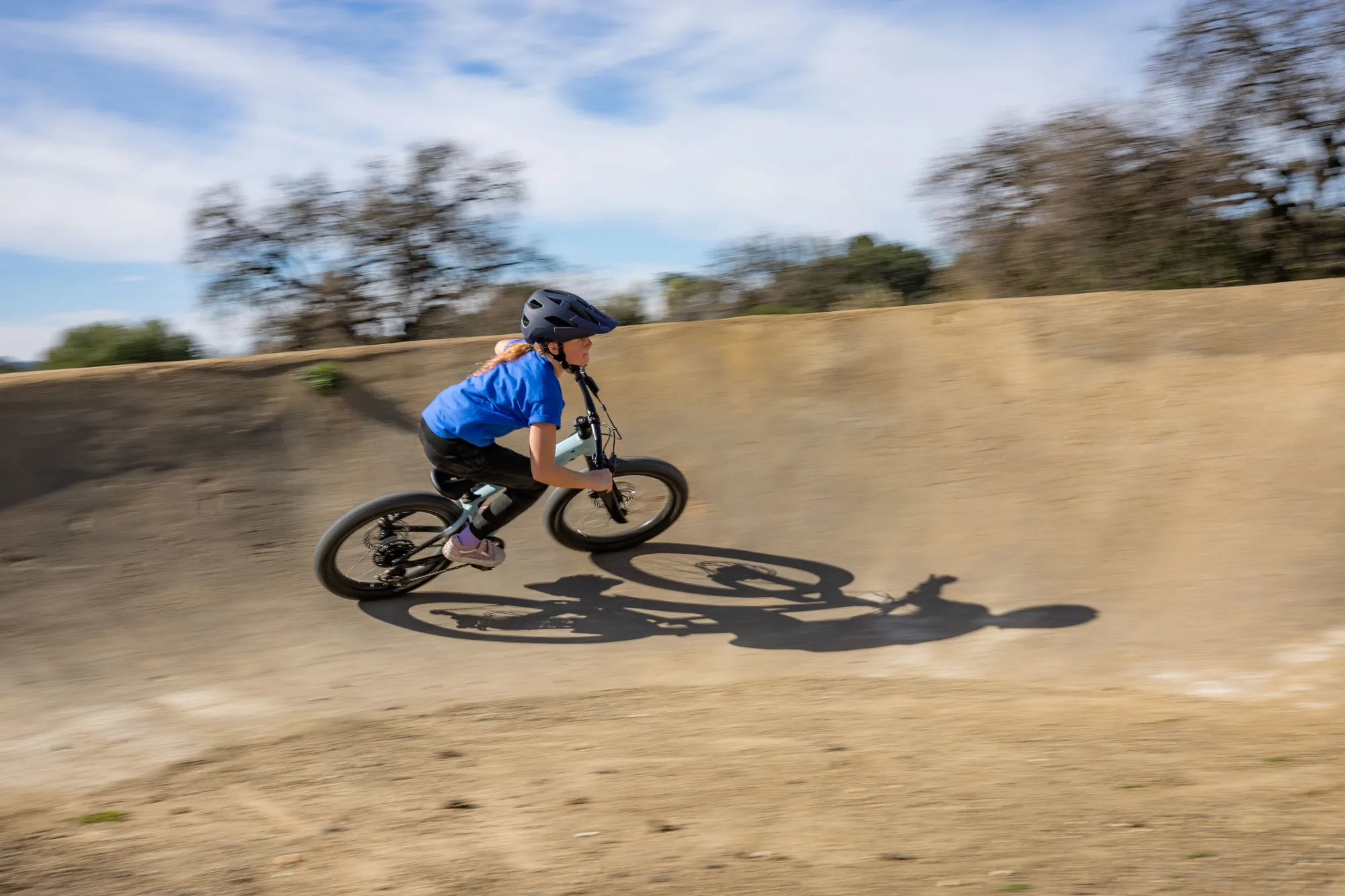 Dítě v přilbě projíždí klopenou zatáčku na pumptracku na kole Liv STP 20