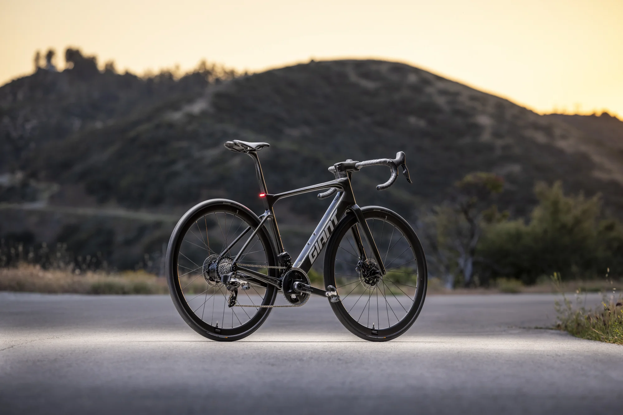 Elektrokolo Giant Defy Advanced E+ Elite stojí na silnici při západu slunce, svítí zadní světlo