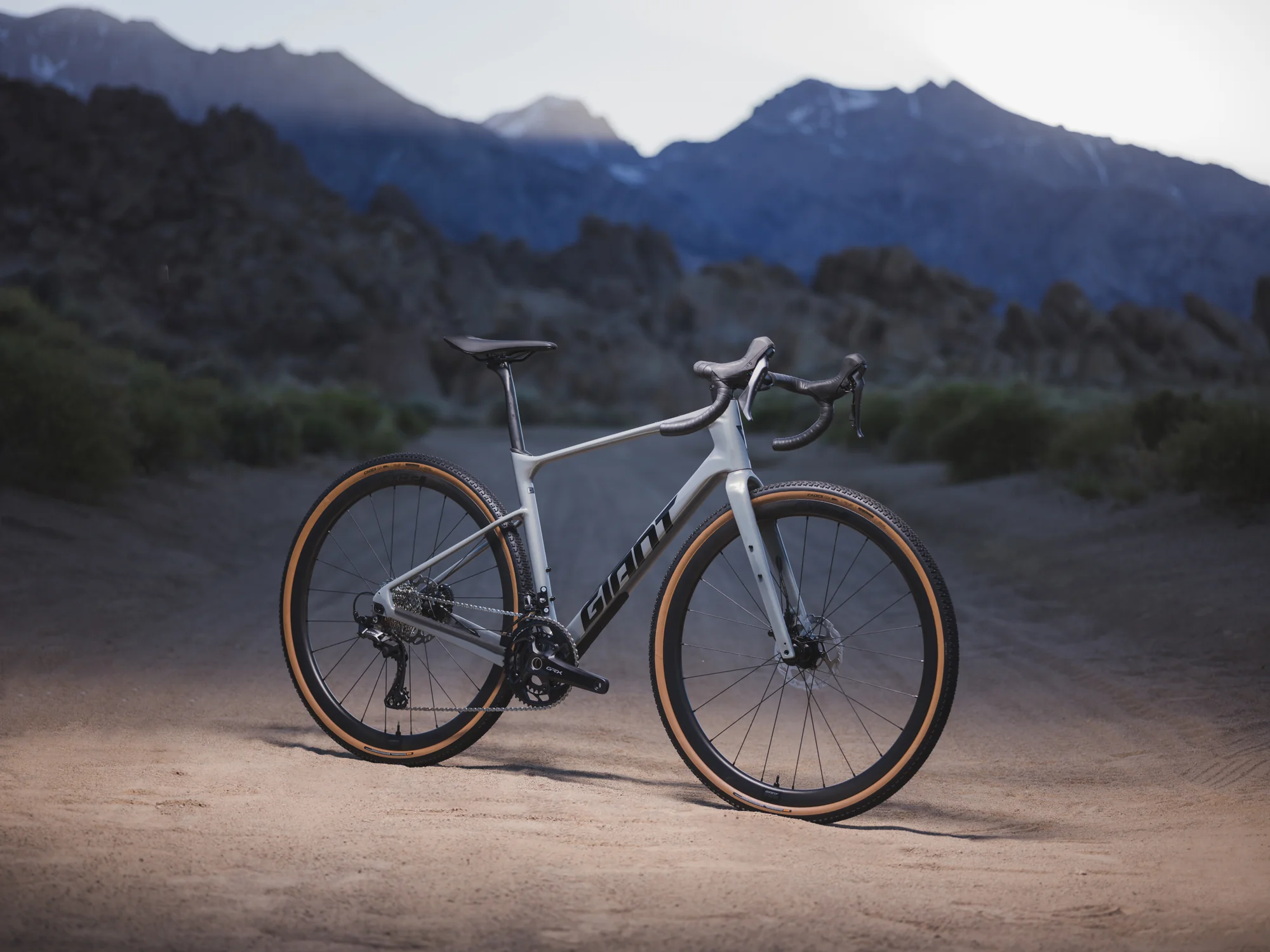 Karbonové gravel kolo Giant Revolt Advanced stojí na šotolinové cestě před horskou siluetou