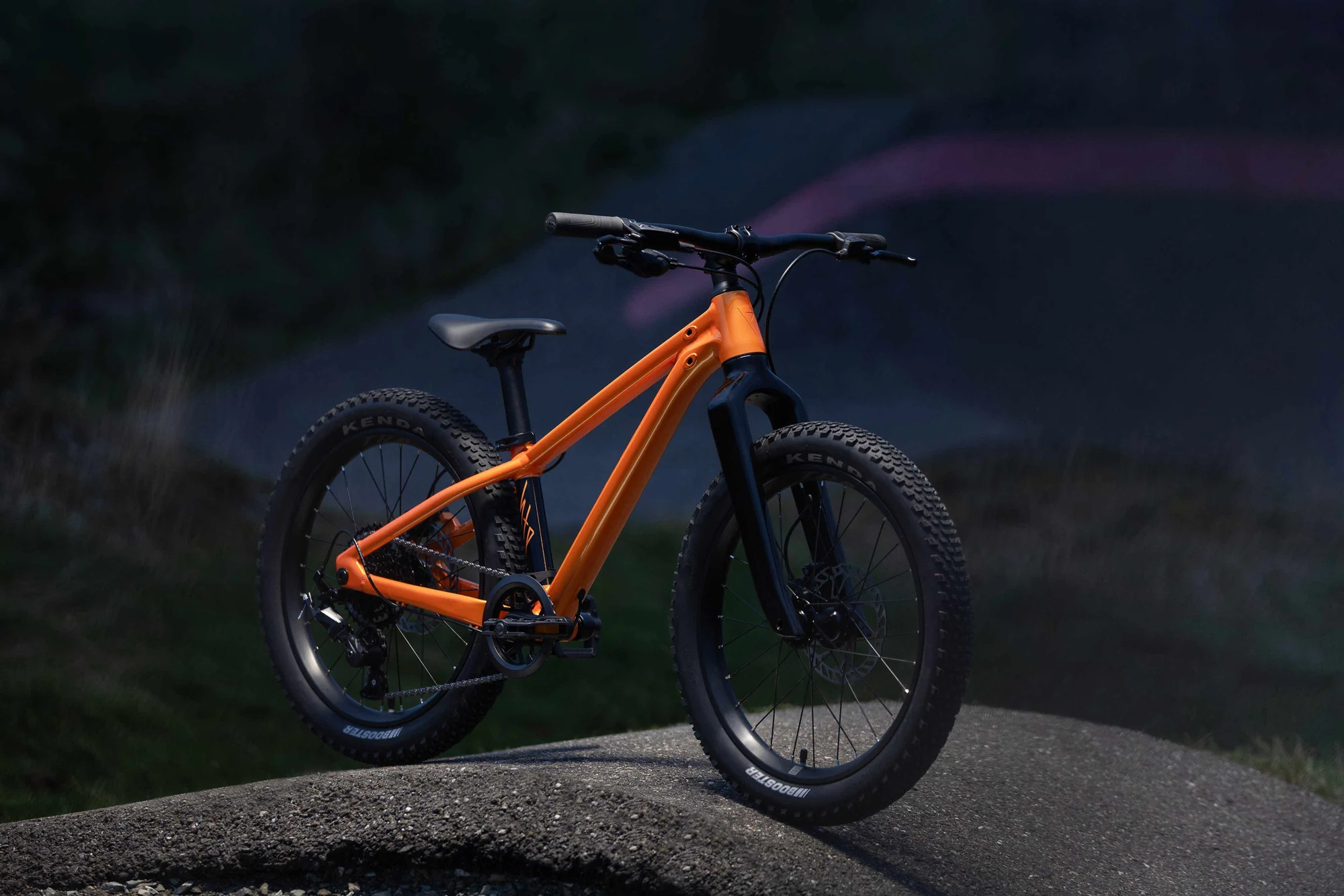 Giant STP 20 v barvě Metallic Orange stojí na zemním pumptracku, pohled zepředu za soumraku