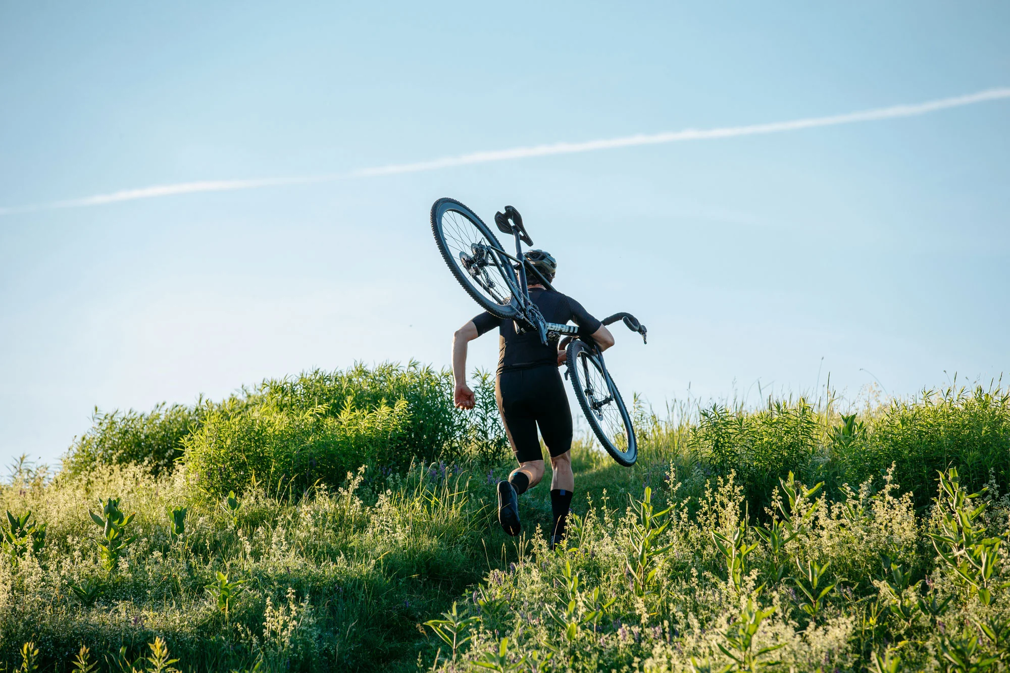 Cyklista nese kolo Giant TCX Advanced Pro na rameni po travnatém svahu