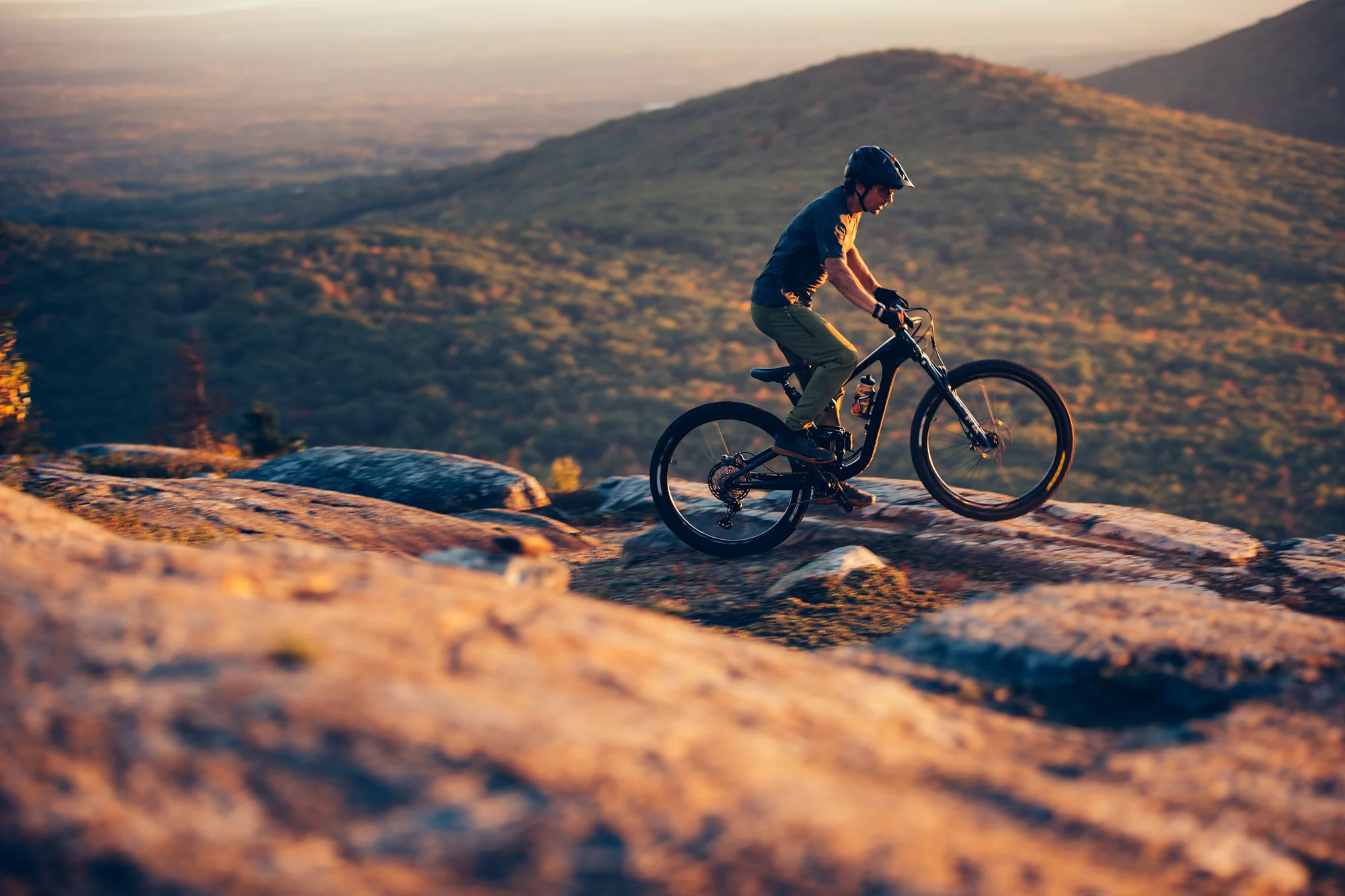 Jezdec na kole Giant Trance Advanced Pro 29 sjíždí skalnatý hřeben při západu slunce