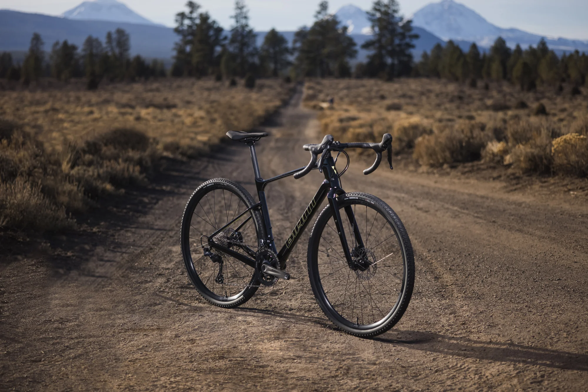 Karbonový gravel Giant Revolt Advanced stojí na šotolinové cestě s horami v pozadí