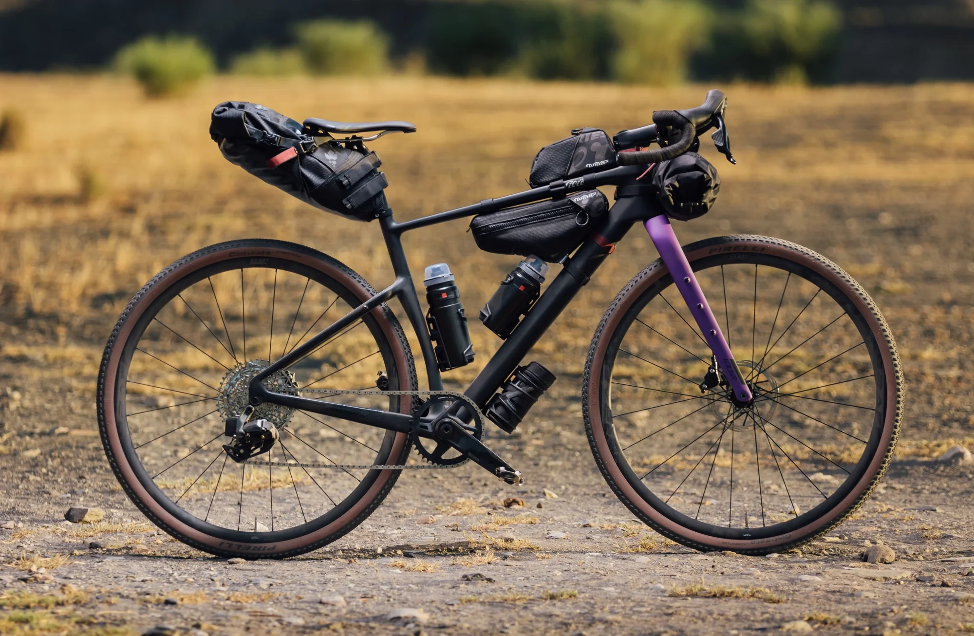 Wilier Adlar v barvě Black Purple s brašnami na rámu, řídítkách a pod sedlem na suché pláni