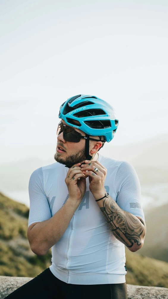 Jezdec si v helmě KASK Protone Icon zapíná podbradní řemínek, v pozadí kopce