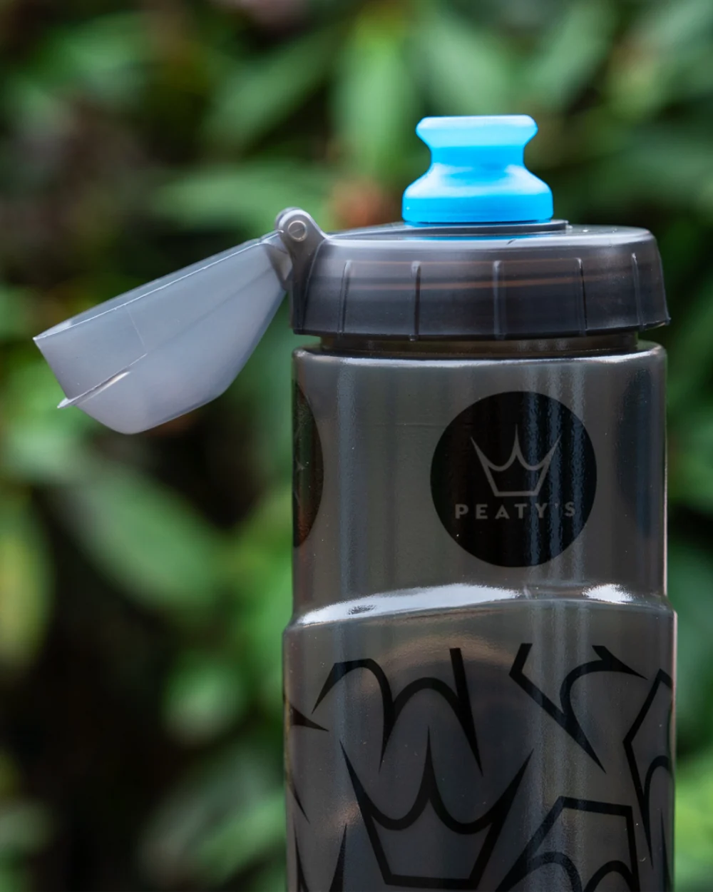 Detail lahve Peaty's x Fidlock Lockin s odklopenou krytkou Dirt Cap nad modrým náustkem