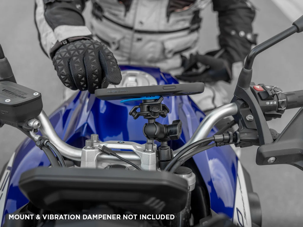 Ruka v rukavici u telefonu v pouzdře Quad Lock nasazeného na šířku nad nádrží modrého motocyklu, pod ním adaptér s tlumičem vibrací v rameni (pouzdro, tlumič vibrací a rameno se prodávají zvlášť)