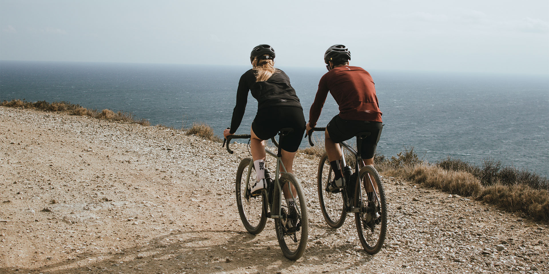 Dva cyklisté na gravelových kolech na šotolinové cestě nad mořem