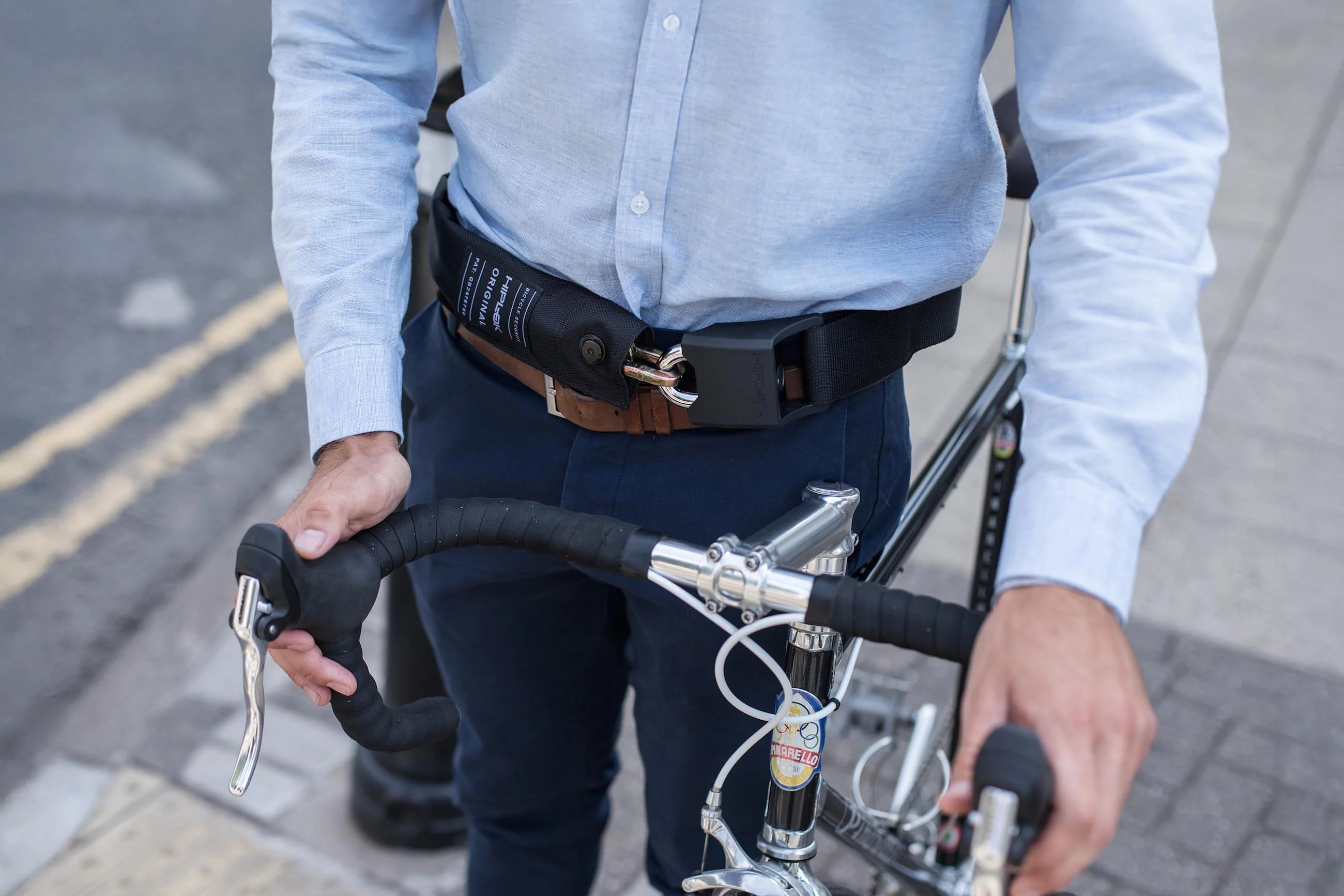 Cyklista s řetězovým zámkem Hiplok Original zapnutým kolem pasu drží řídítka silničního kola