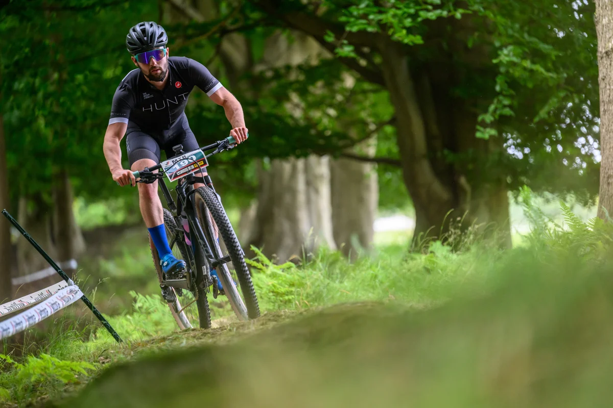 Závodník v dresu HUNT na XC horském kole s koly HUNT Race XC MTB 29 projíždí lesní trať