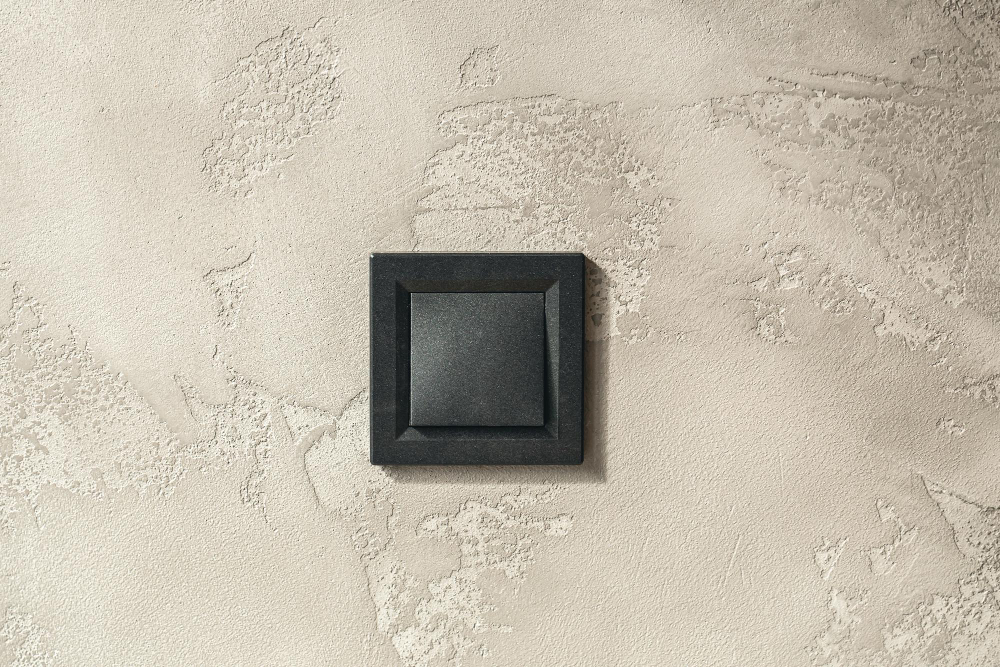 Detail strukturované vnitřní omítky s vypínačem na zdi – povrch může být jádrová, štuková, sádrová nebo vápenná omítka.