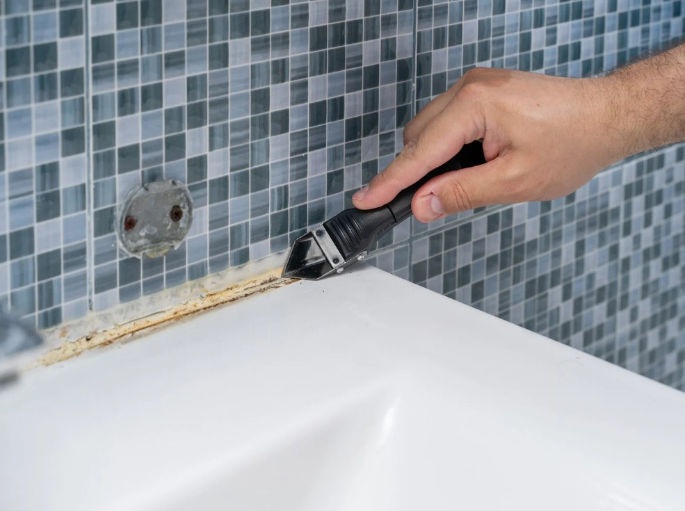 Odřezávání starého silikonu mezi vanou a obkladem pomocí odlamovacího nože.