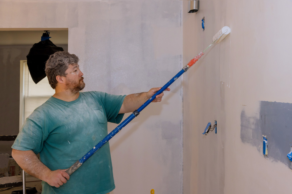 Nanášení penetračního nátěru pod omítku válečkem při přípravě zdi před omítáním.