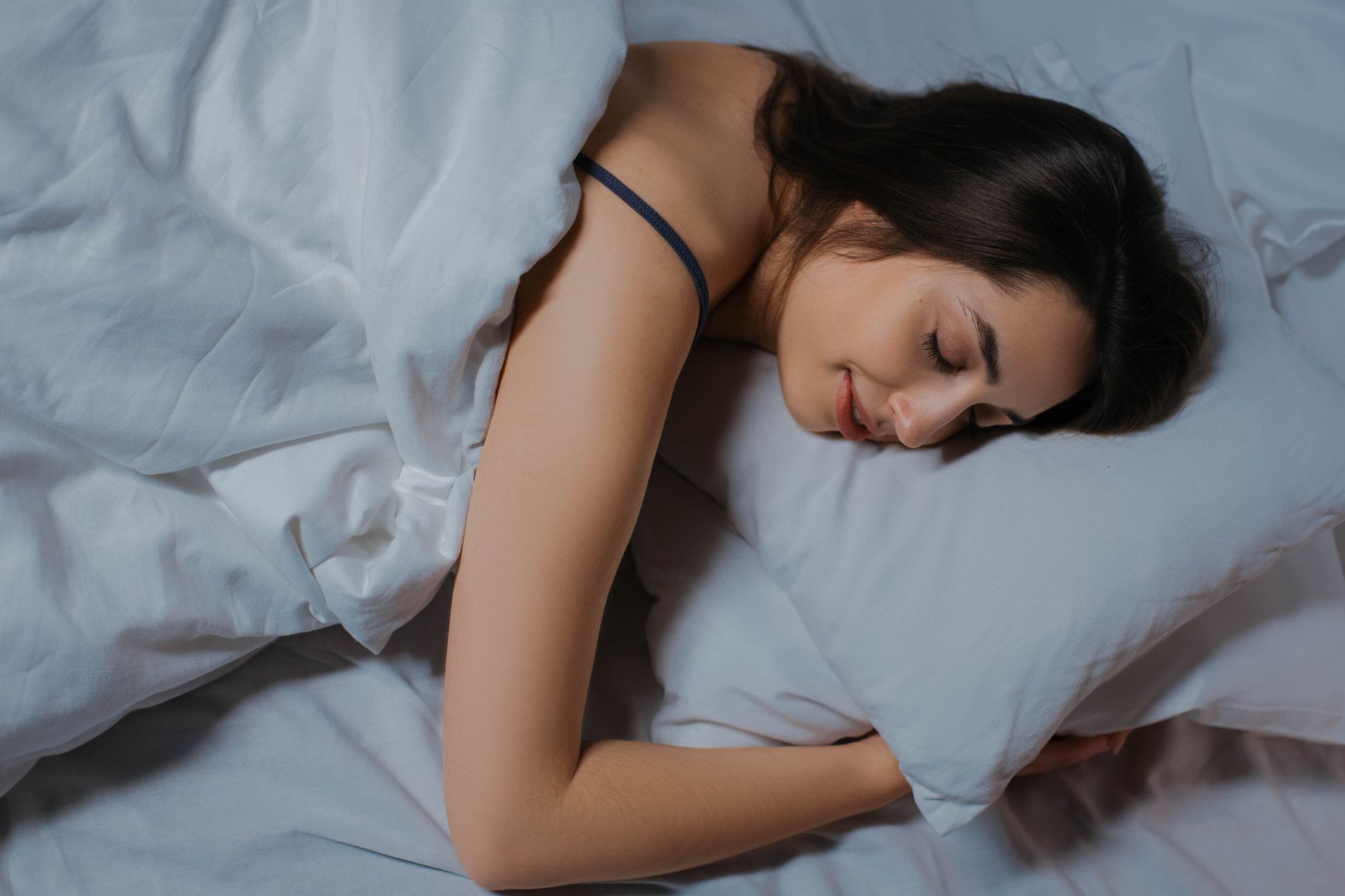 Žena pokojne spí v posteli s bielou posteľnou bielizňou