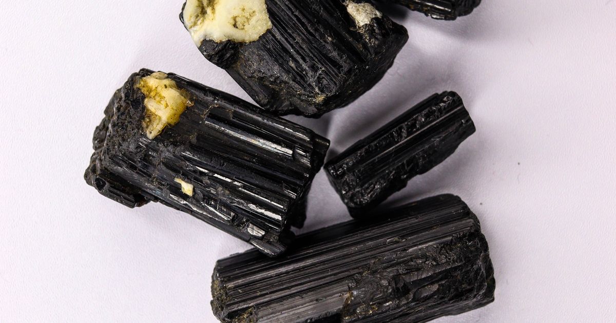 Čierny turmalín (škorl) – surové aj leštené čierne kryštály minerálu na svetlom podklade