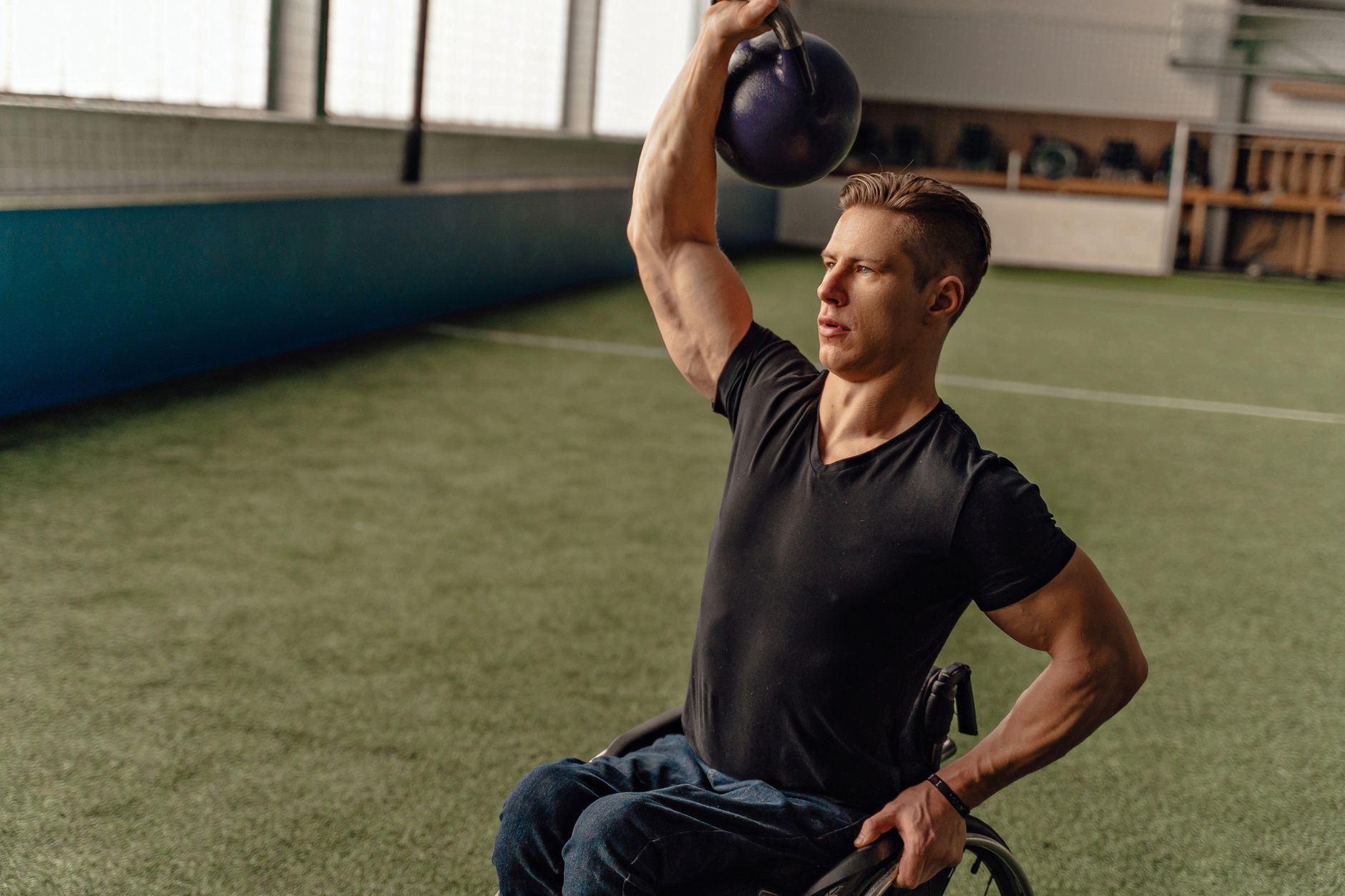Športovec na mechanickom vozíku dvíha kettlebell v hale
