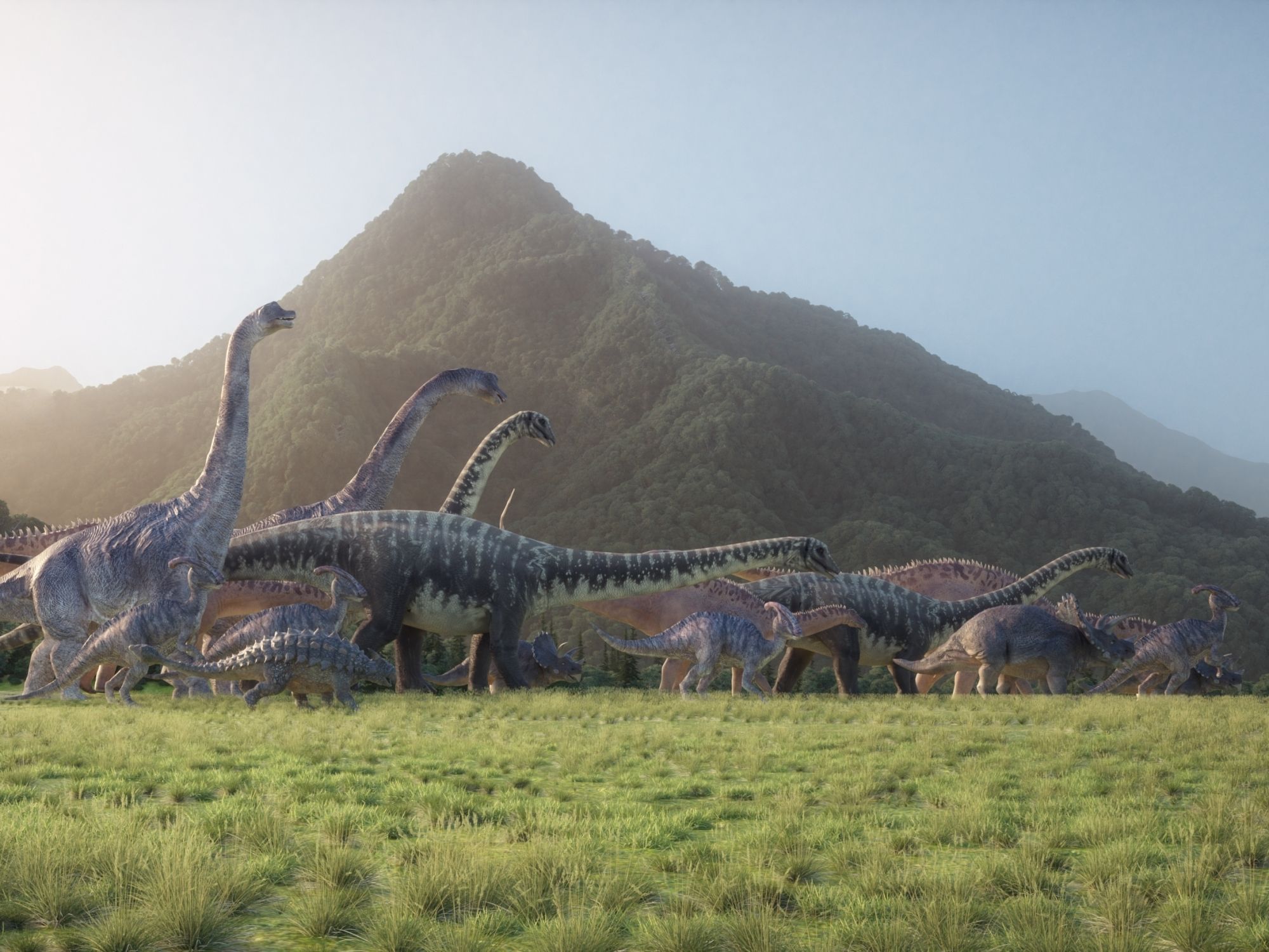 Různí dinosauři kráčející pravěkou krajinou s vegetací a vzdálenými horami.