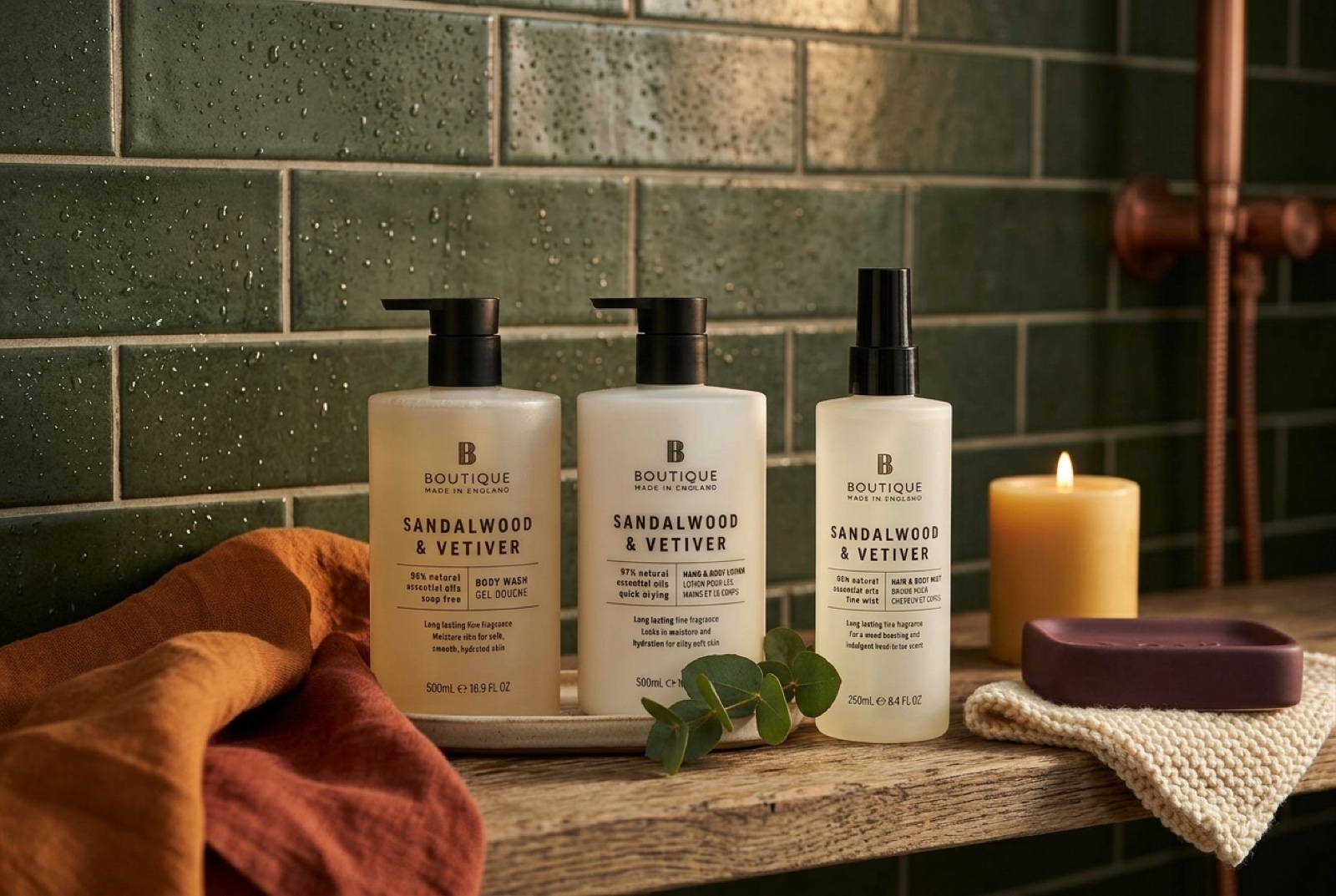 Sprchový gél, telové mlieko a hmla na telo Sandalwood & Vetiver od Boutique na drevenej poličke v sprche so zelenými obkladmi