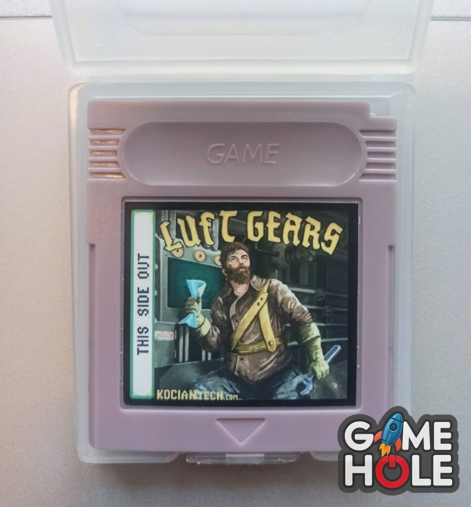 Fialová kazeta hry Luft Gears pro Game Boy v průhledné krabičce, na štítku vousatý mechanik v dieselpunkové dílně