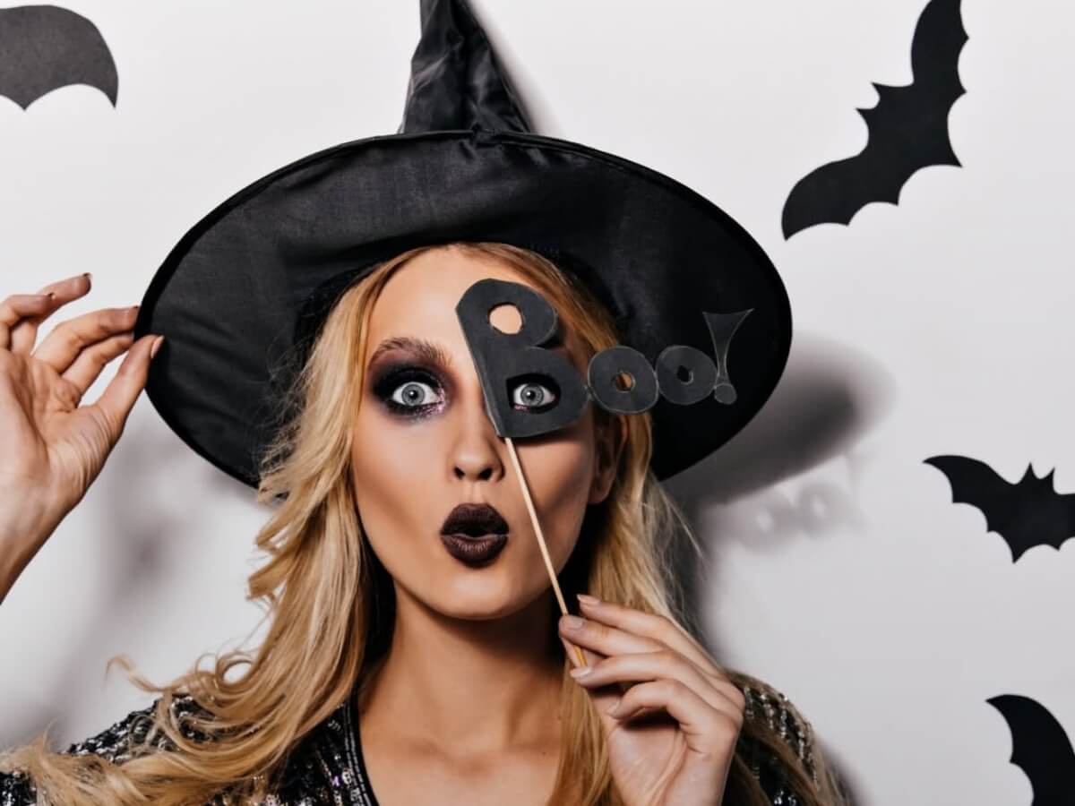 Žena v čarodějnickém klobouku s halloweenským líčením a doplňky.