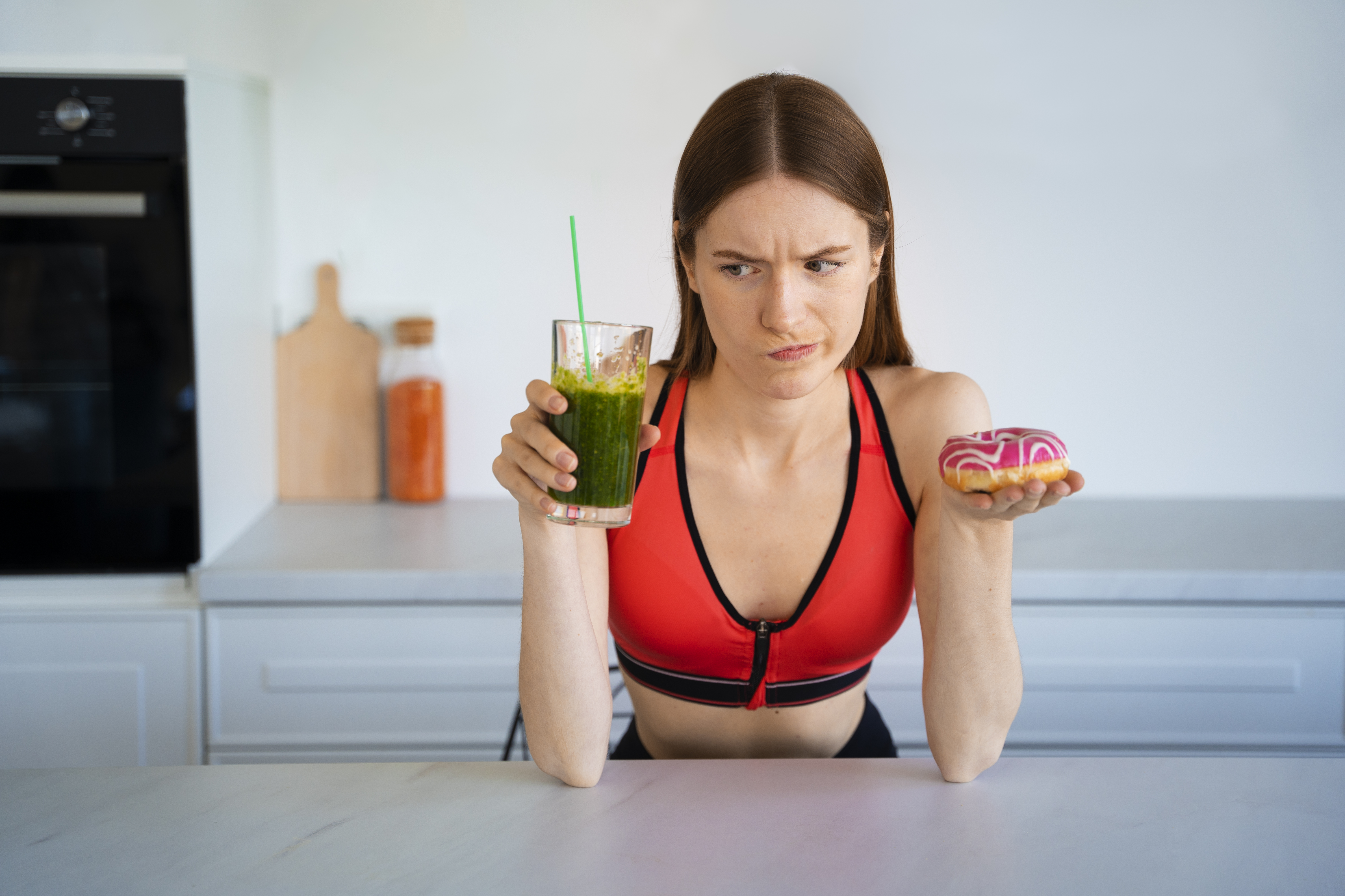 žena v kuchyni má v jednej ruke smoothie a v druhej donut