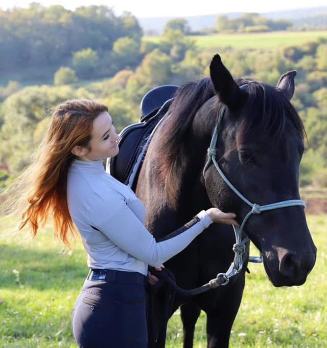 Laura drží koňa za ručne pletenú ohlávku parelku počas prípravy na jazdenie