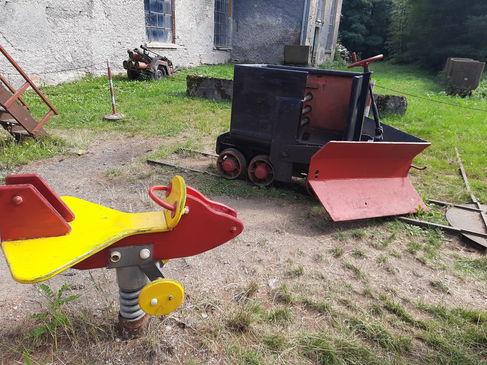 Malá důlní lokomotiva, pluh a dětské houpadlo v areálu v Mladějově