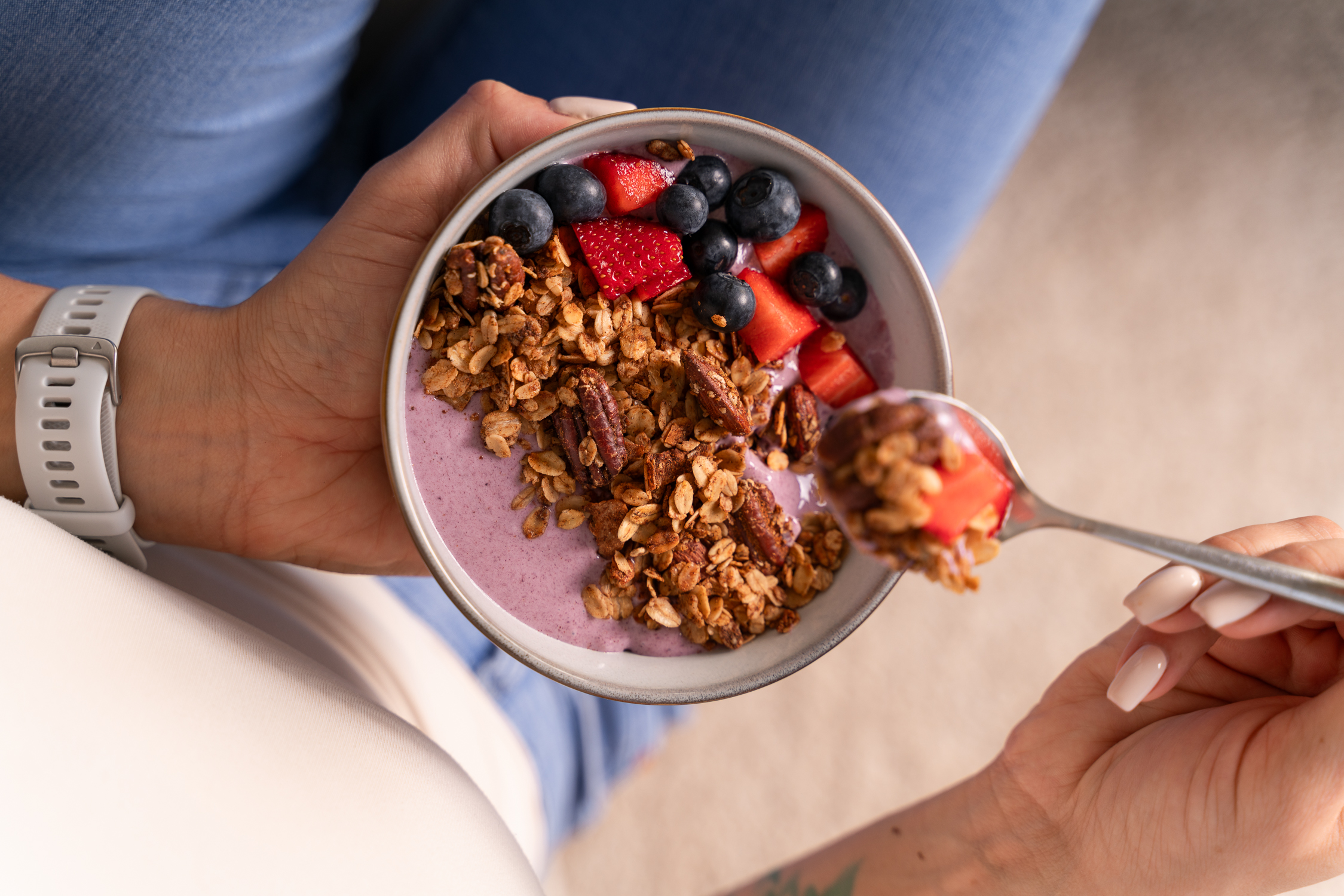 Sedící žena drží v ruce misku s granolou, jogurtem a čerstvým ovocem
