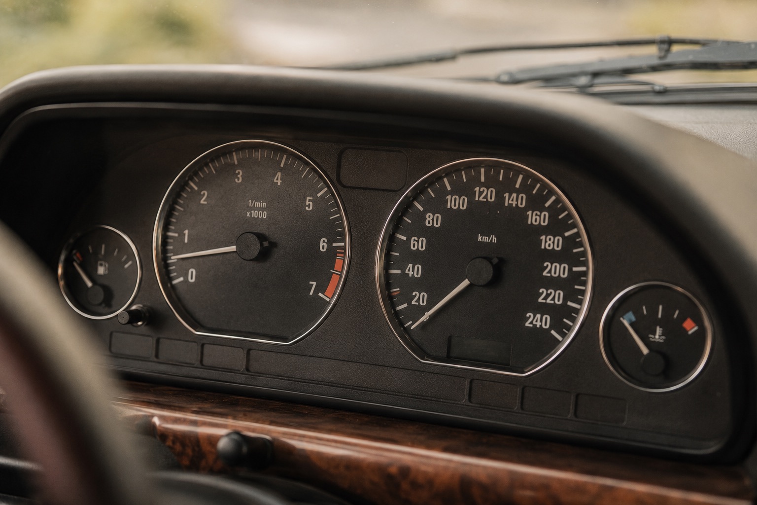 Close-up analógového palubného panelu vintage auta z 90. rokov so starostlivo zachovaným tachometrom, otáčkomerom a chrómovými detailmi. Estetika éry prezentuje autenticitu historického vozidla.