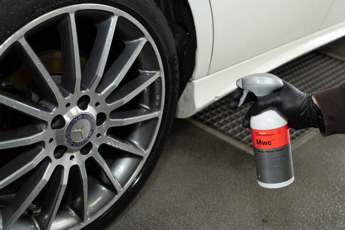Ruka v nitrilovej rukavici drží čistič diskov Koch Chemie Magic Wheel Cleaner pri hliníkovom disku auta.