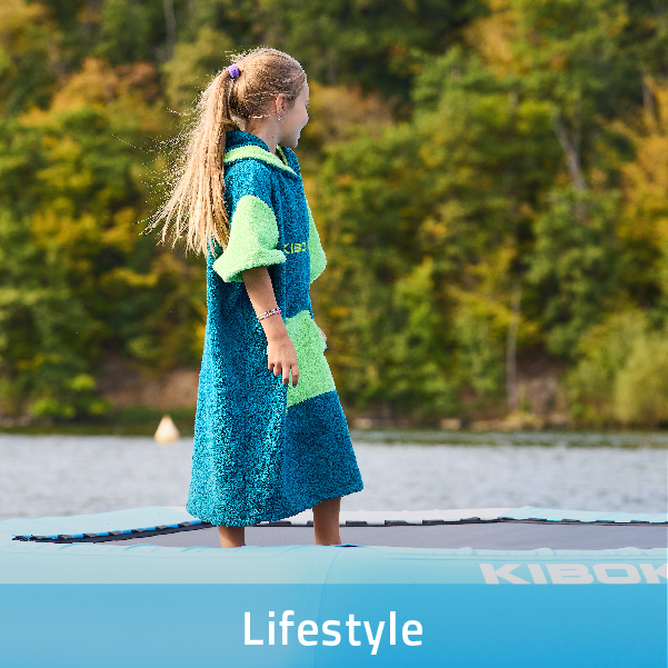 Veselá holčička stojící na vodní trampolíně, oblečená do stylového poncha Kiboko