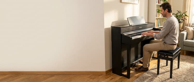 Muž, který hraje na hnědé digitální piano v bytě.
