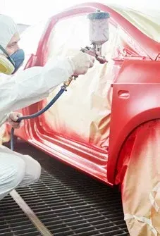 Lakýrník stříkací pistolí nanáší barvu na karoserii v lakovně