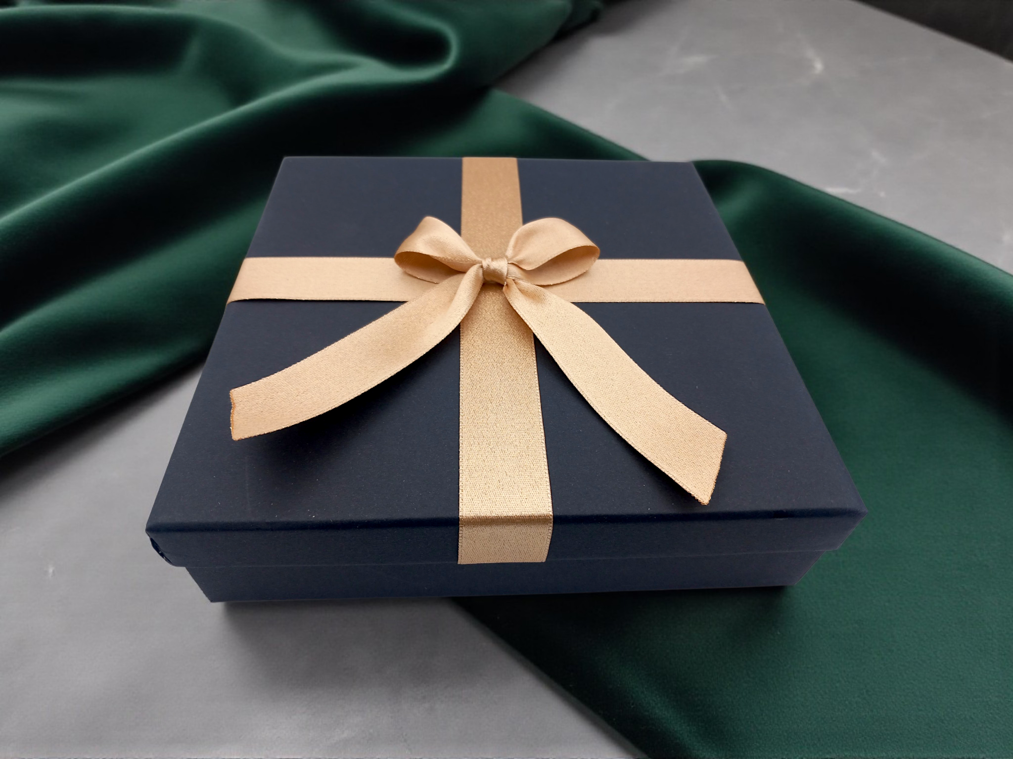 Elegantní černá dárková krabička se zlatou mašlí na zeleném saténu