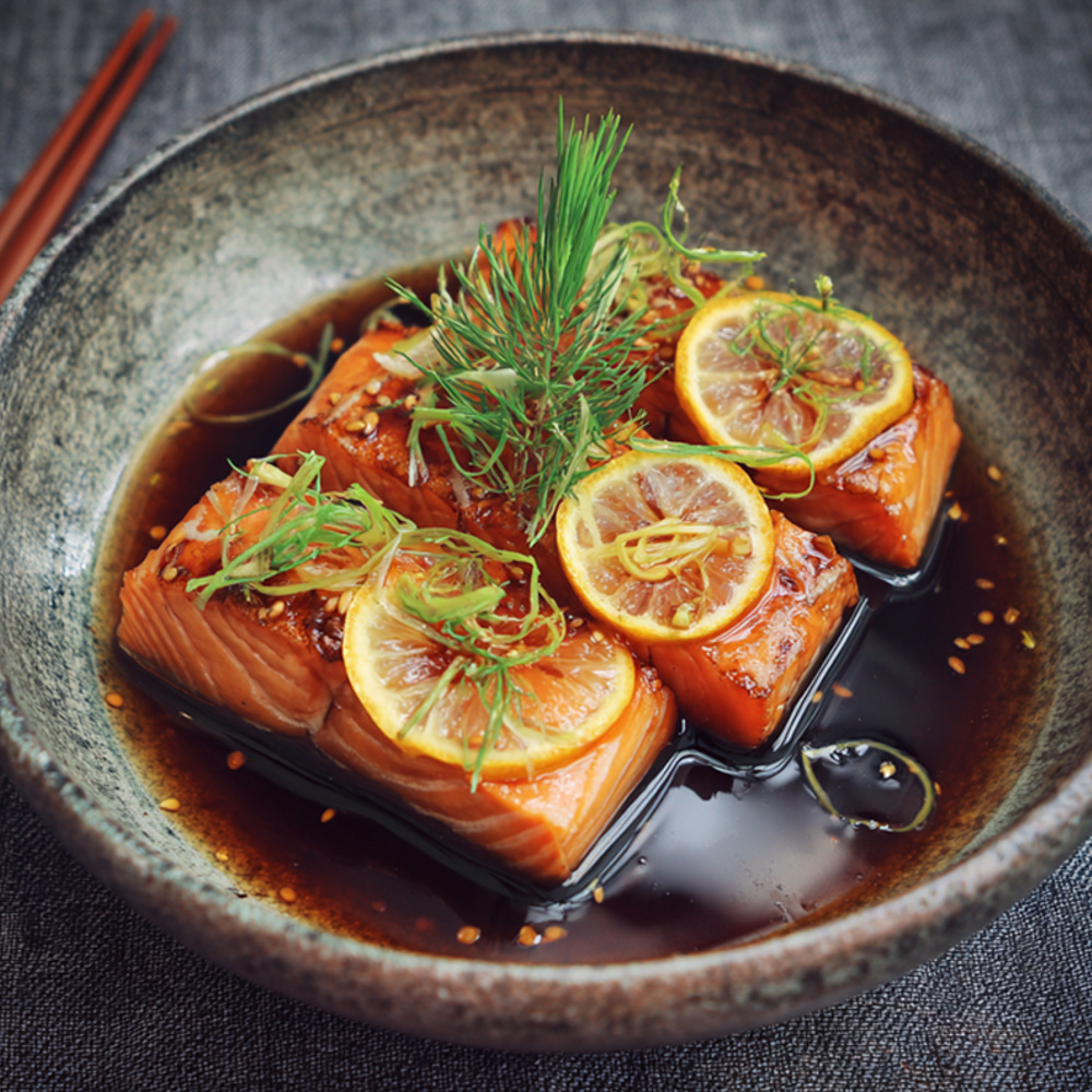 Marinovaný losos v sójovo‑yuzu omáčce v elegantní misce; na filetu plátek yuzu a zelený lístek, lesklá omáčka podtrhuje spojení sójové chuti a citrusové svěžesti KOTSAM Yuzu