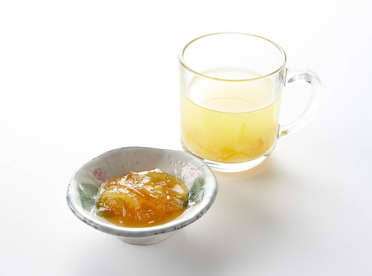 Čaj z yuzu vedle yuzu marmelády na bílém pozadí