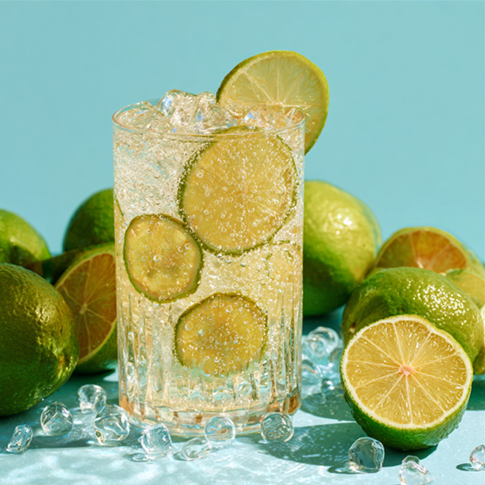 Šumivý nápoj ze zelené mandarinky s ledem; sklenice dekorovaná plátky zelené mandarinky, kostky ledu okolo.