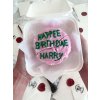 Dekorativní svíčka ve tvaru dortu s růžovou polevou a nápisem Happee Birthdae Harry, inspirovaná dortem od Hagrida pro Harry Pottera.