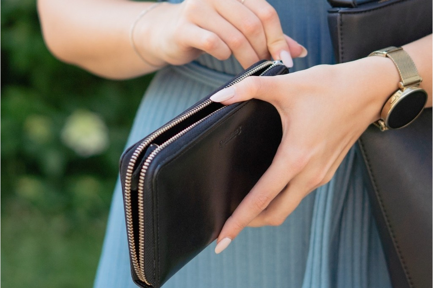 Ruka rozepíná obvodový zip YKK na černé peněžence Donna