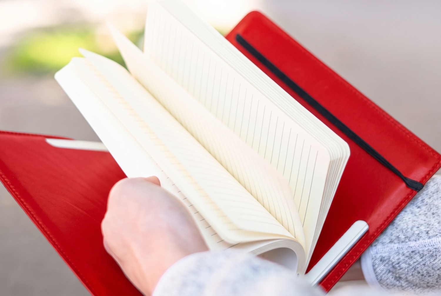 Ruce listují otevřeným linkovaným zápisníkem v červeném koženém obalu Eduard venku