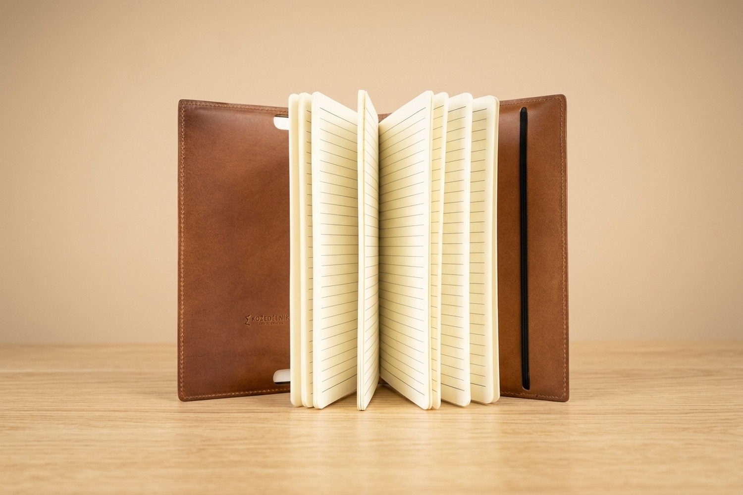 Koňakový kožený zápisník Eduard stojící otevřený s rozevřenými linkovanými stránkami na dubovém stole