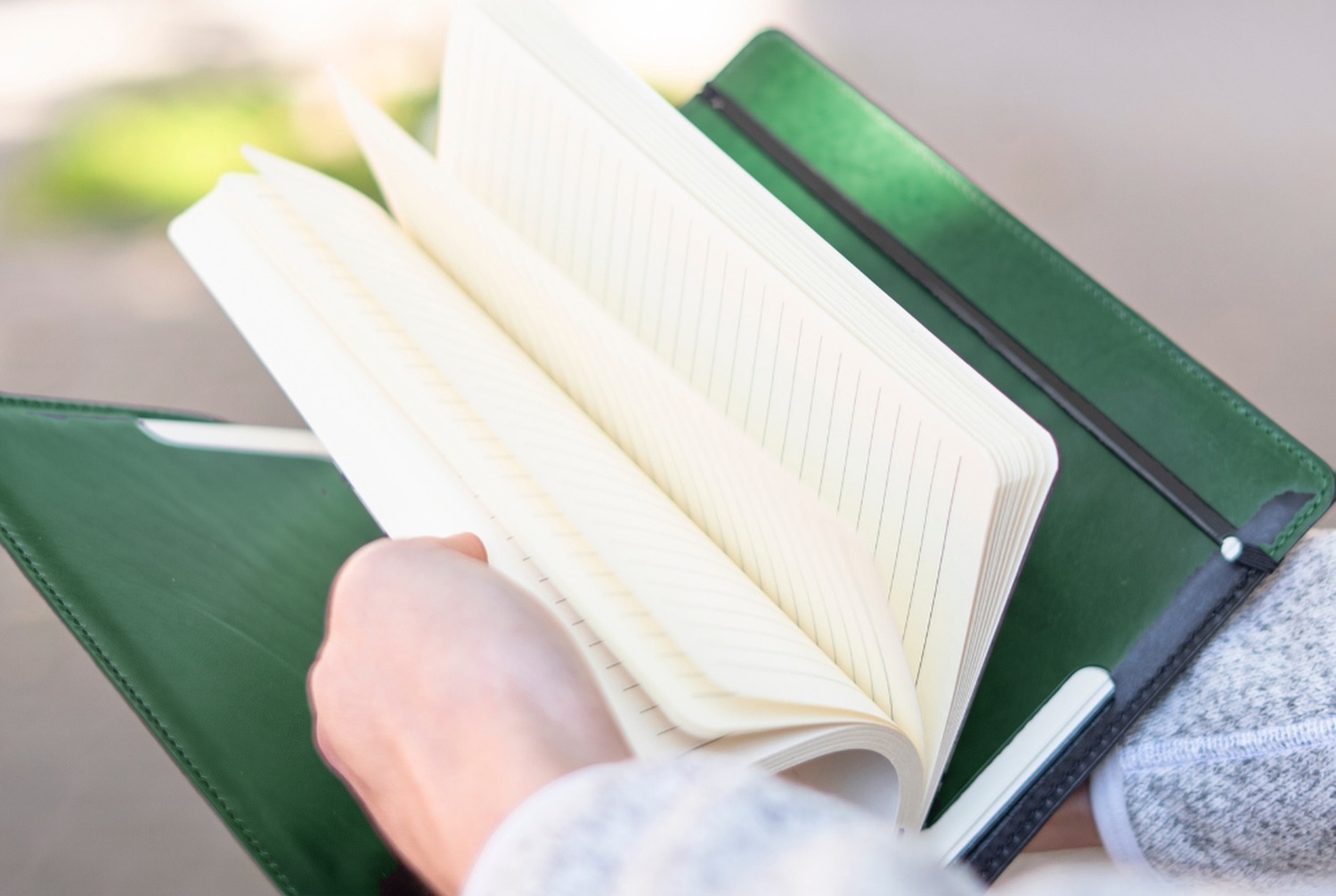 Ruce listují otevřeným linkovaným zápisníkem v zeleném koženém obalu Eduard venku